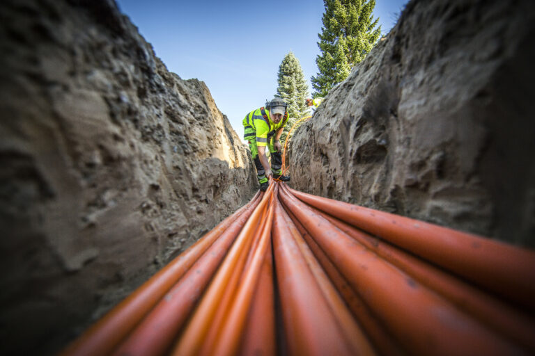 Montør legger oransje fiberkabler i en oppgravd grøft