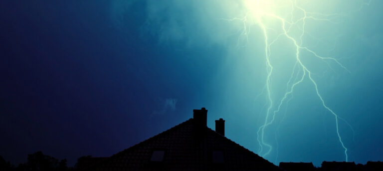 Lynnedslag over mørk himmel. Et hustak vises nederst på bildet.